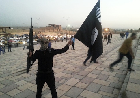 A fighter of the ISIL holds a flag and a weapon on a street in Mosul