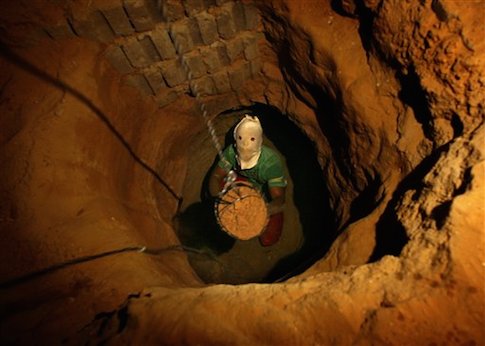 A Palestinian tunnel digger, wearing a mask to conceal his identity, removes sand in a bucket from a tunnel underground in Rafah, in the southern Gaza Strip