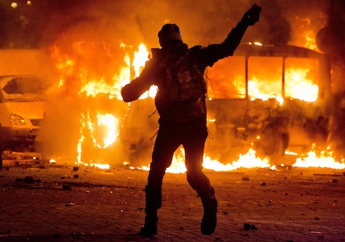A protester throws a stone towards a burning police bus