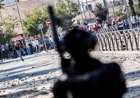 A Palestinian protester is hurling stones at Israeli policemen.