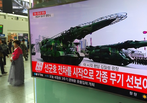 People walk past a television screen broadcasting live footage of a parade to mark the 105th anniversary of the birth of North Korea's founder Kim Il-Sung
