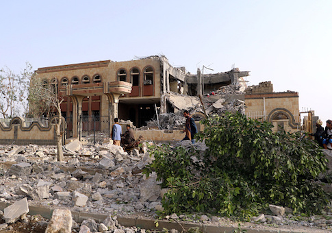 Yemenis walk past a building, housing branches of the Finance Ministry and Central Bank, that was heavily damaged in an airstrike by the Saudi-led coalition