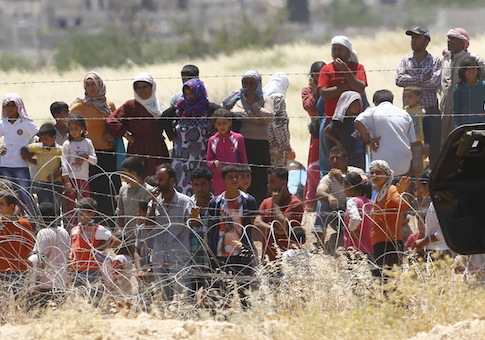 Syrian Kurds from Kobani wait behind the border fences to cross into Turkey as they are pictured from the Turkish border town of Suruc in Sanliurfa province, Turkey