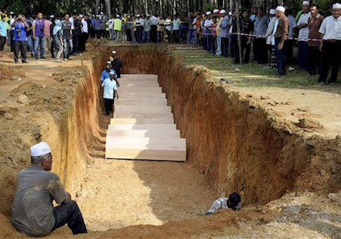 Malaysian religious officers and villagers place coffins containing remains of Rohingya migrants for a mass burial ceremony in Kedah, Malaysia Monday, June 22