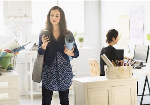 Businesswoman carrying yoga mat and cell phone in office