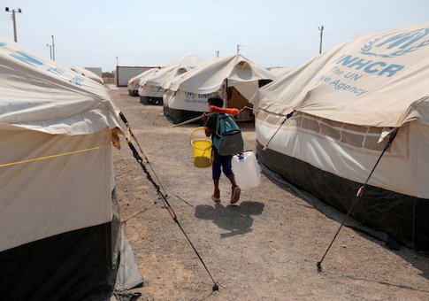 FILE PHOTO: A Venezuelan migrant child carries a broom and a bucket while he walks in a camp run by the UN refugee agency UNHCR in Maicao