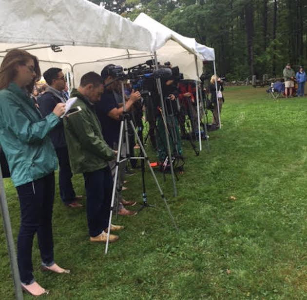 Kesnetz, wearing a green coat, films remembrance ceremony from under tent