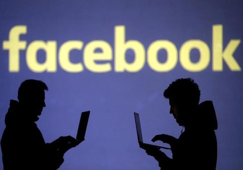 Silhouettes of laptop users are seen next to a screen projection of Facebook logo in this picture illustration